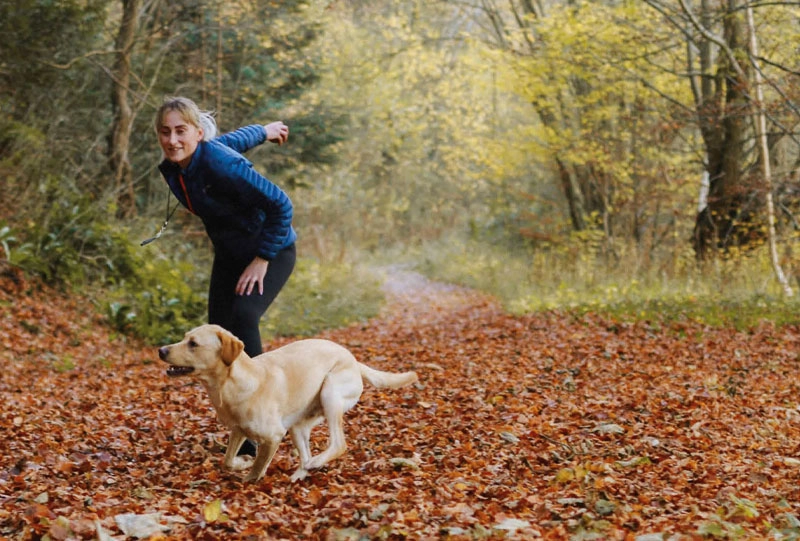 Frau spielt mit Hund in einem herbstlichen Wald